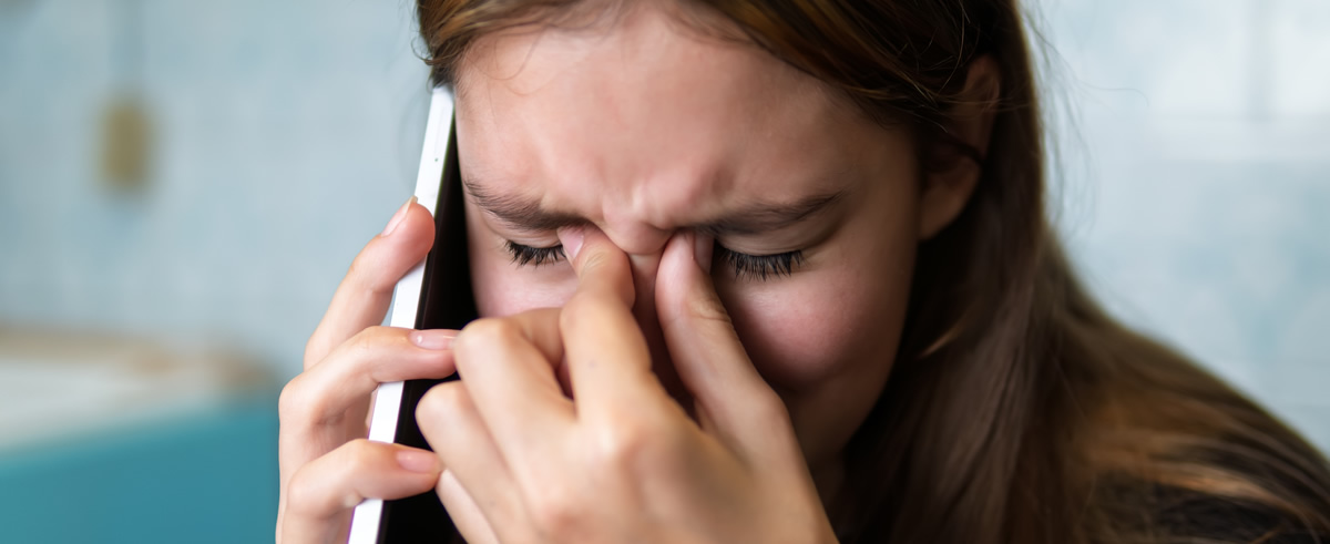 Ein Mädchen hält ein Telefon ans Ohr und verzieht vor Stress oder Kummer das Gesicht, während sie sich die Nasenwurzel reibt.