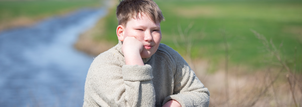 Ein Junge sitzt im Freien auf einem Stein und stützt nachdenklich den Kopf auf seine Hand.