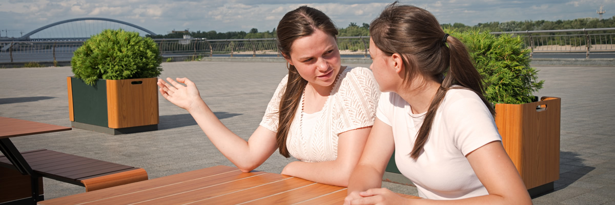 Zwei junge Frauen sitzen draußen an einem Tisch und führen ein angeregtes Gespräch miteinander.