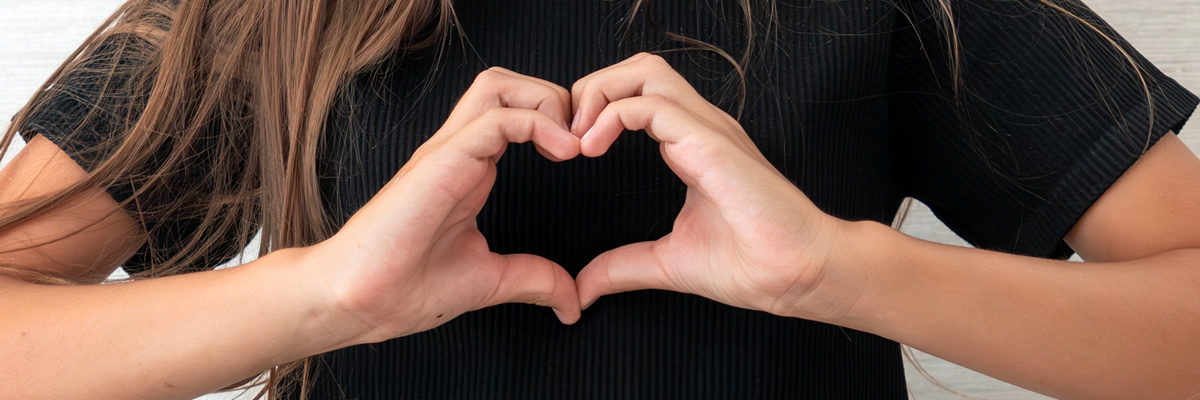 Eine Person formt mit beiden Händen ein Herz vor ihrem Oberkörper.